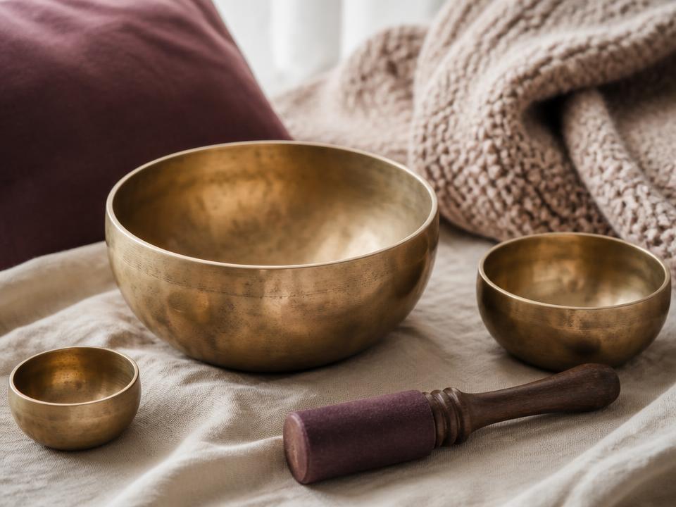 Brass singing bowls and a mallet resting on soft cream linen